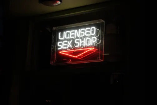 Letrero de neón «Licensed Sex Shop» con luz blanca y roja sobre fondo negro