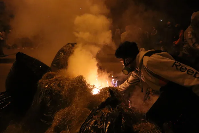 Manifestante con el rostro cubierto prende fuego a llantas y objetos en una barricada