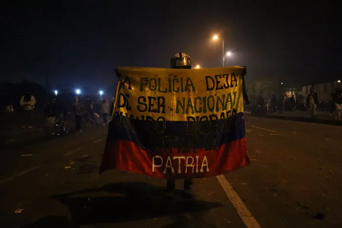 Manifestantes sostienen una bandera de Colombia con un mensaje contra la policía en una calle nocturna