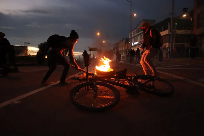 Manifestantes alrededor de una bicicleta tirada junto a una fogata en una avenida al anochecer
