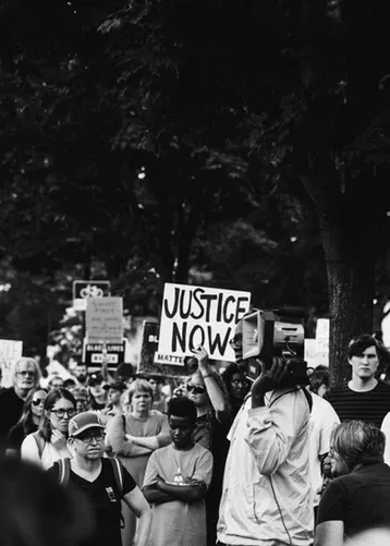 Manifestantes en blanco y negro con carteles, uno de ellos con el lema «Justice now»