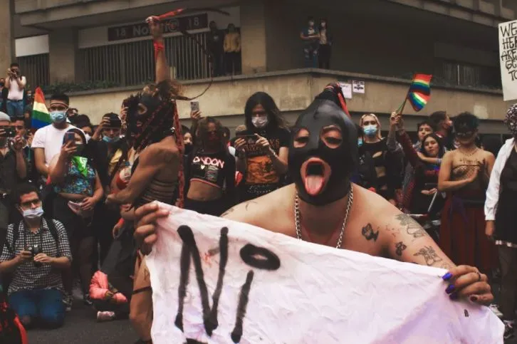 Manifestantes encapuchados sostienen una pancarta blanca con la palabra «Ni» en la marcha del orgullo de Medellín