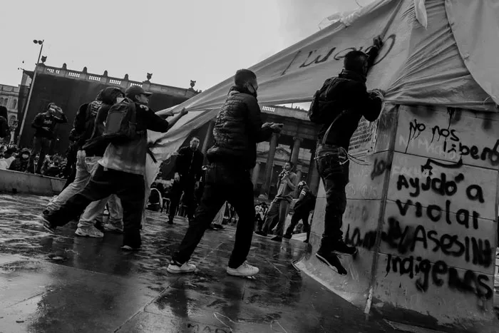 Manifestantes junto a un muro con grafitis y una carpa rota durante un enfrentamiento bajo la lluvia