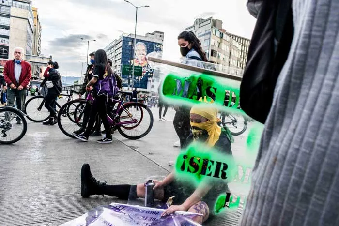 Manifestantes con pancartas de letras verdes en una calle, con ciclistas y peatones al fondo