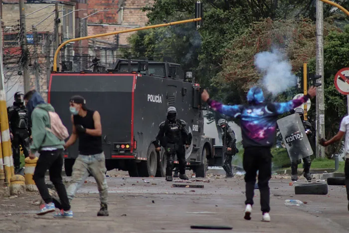 Manifestantes lanzan objetos frente a policías antidisturbios y un vehículo blindado en una calle de Colombia