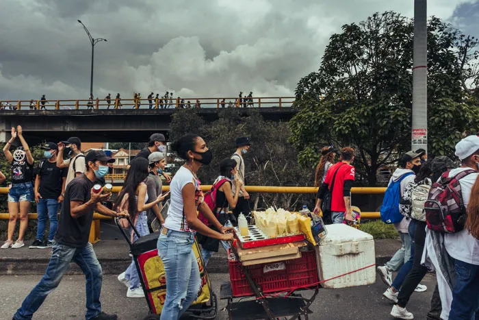 Manifestantes y vendedores con carritos ambulantes caminan por una calle bajo un puente