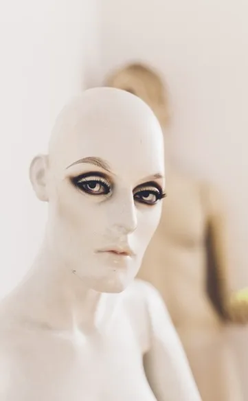 Maniquí calvo con maquillaje oscuro en los ojos junto a otro maniquí de una tienda de ropa