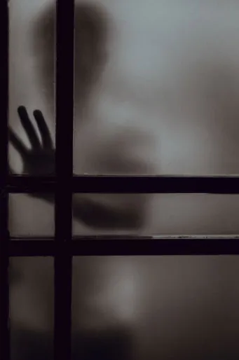 Silueta de una mano apoyada contra un vidrio empañado con barrotes oscuros