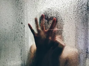 Mano sobre un vidrio empañado con gotas de agua, con una silueta detrás