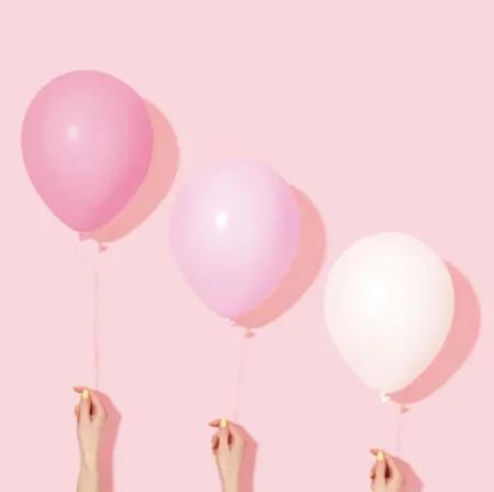 Manos sostienen tres globos rosados y blancos sobre fondo rosa pálido