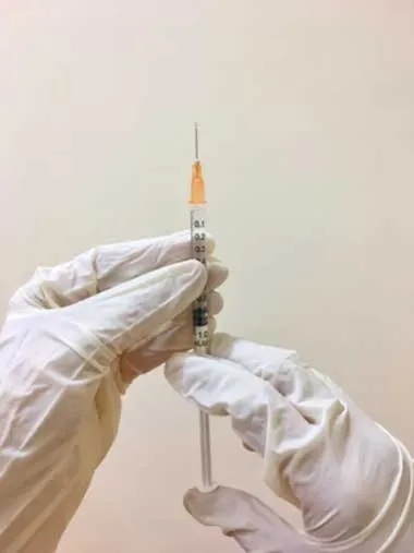 Manos con guantes blancos sostienen una jeringa con aguja lista para aplicar una vacuna