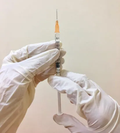Manos con guantes blancos sostienen una jeringa para aplicar una vacuna