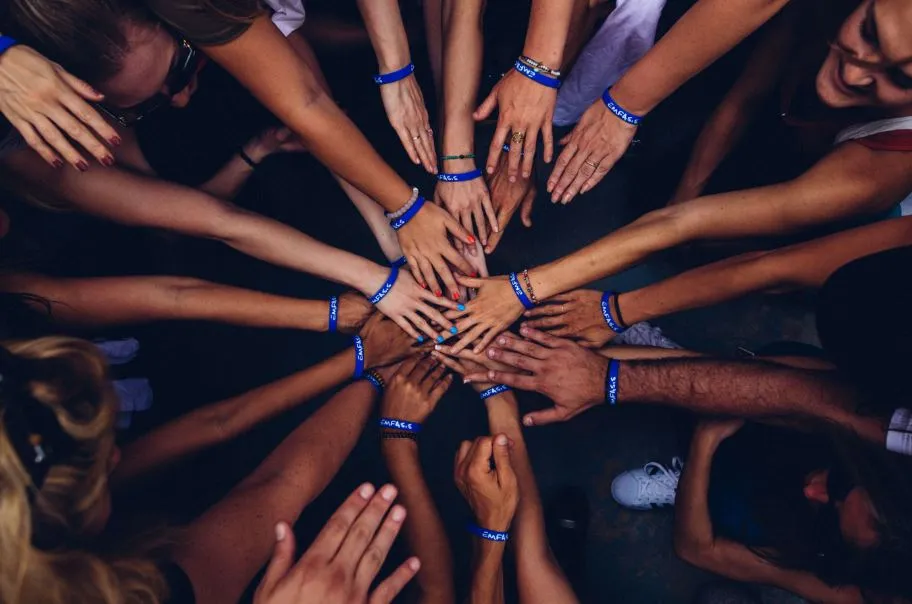 Manos de muchas personas unidas en círculo, con pulseras azules, vistas desde arriba