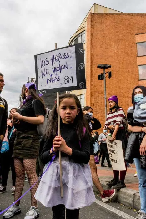 Niña con falda lila sostiene un cartel «Los hombres no matan, nunca» junto a mujeres en la marcha del 8 de marzo de 2021