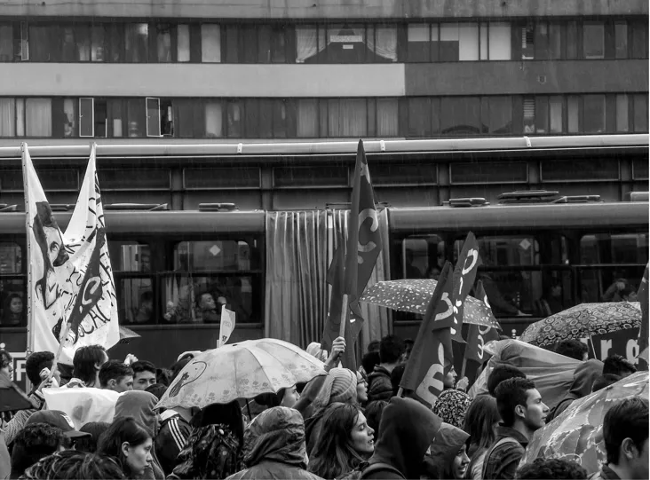Multitud con banderas y paraguas frente a un bus articulado durante la marcha estudiantil en Bogotá