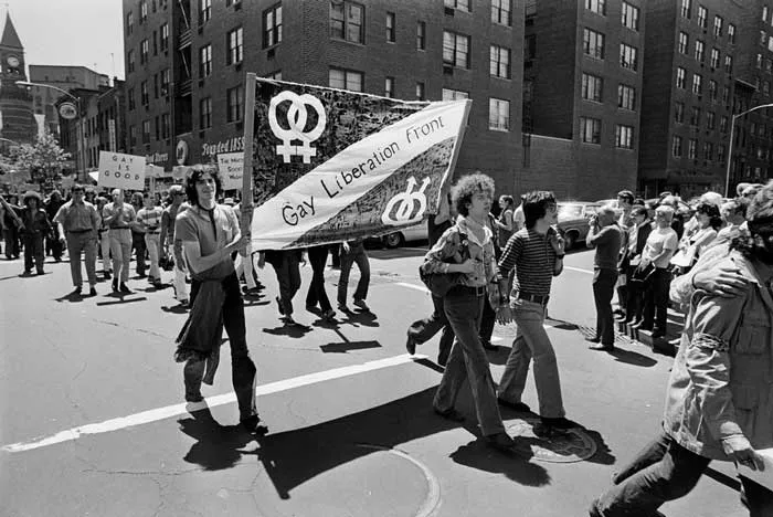 Marcha en blanco y negro con una pancarta del Gay Liberation Front y símbolos de género, en una calle de Nueva York