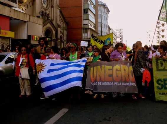 Marcha por una calle de Montevideo con la bandera de Uruguay y una pancarta de organizaciones de mujeres negras