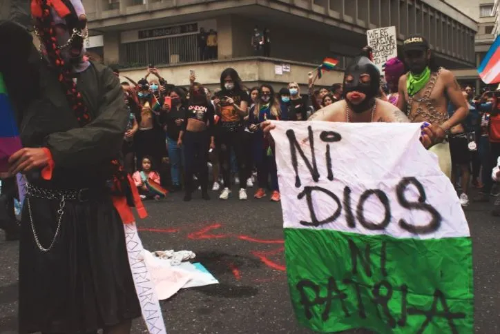 Manifestantes enmascarados sostienen una bandera blanca y verde con el mensaje «Ni Dios ni patria» durante una performance
