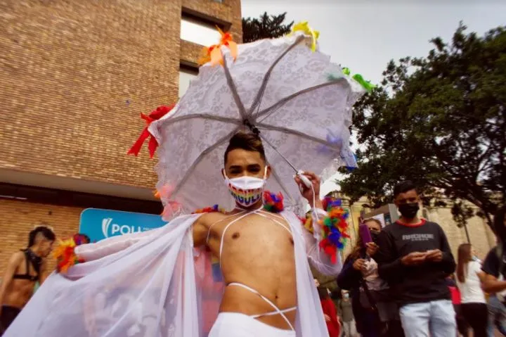 Persona con una capa blanca y una sombrilla de encaje decorada con cintas de colores en la Marcha del Orgullo