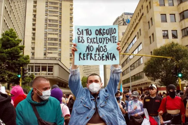 Joven con chaqueta de mezclilla levanta un cartel «Si tu orgullo es excluyente no nos representa» en la Marcha del Orgullo