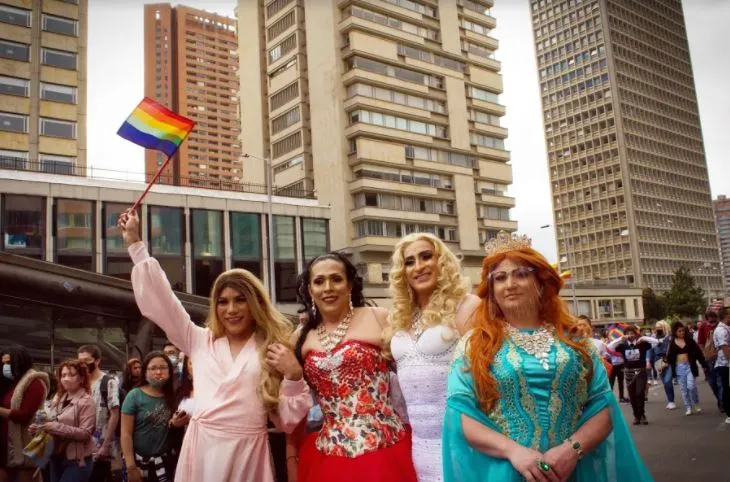 Cuatro mujeres con vestidos de gala posan en la Marcha del Orgullo, una de ellas con una bandera arcoíris