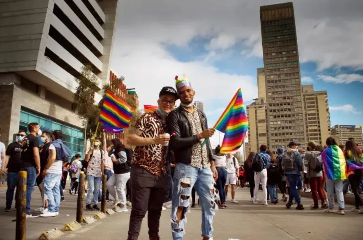 Dos personas posan con banderas arcoíris en una calle de la Marcha del Orgullo, entre la multitud