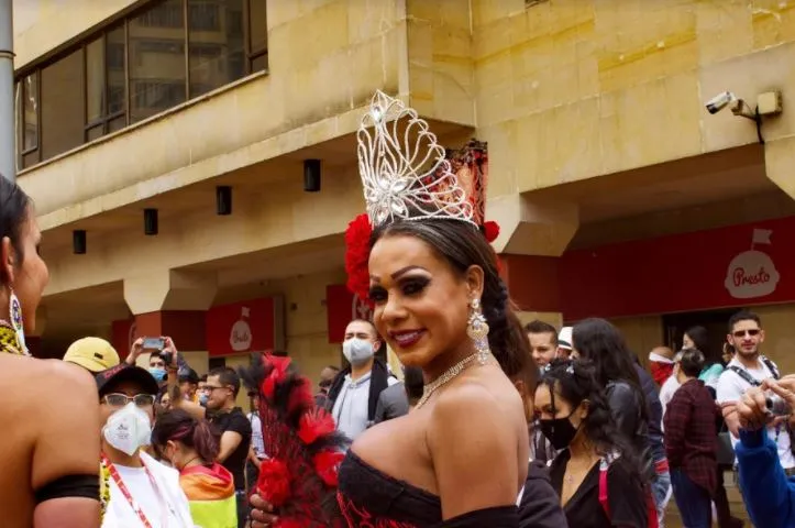 Mujer sonriente con corona plateada y vestido rojo escotado entre la multitud de la Marcha del Orgullo