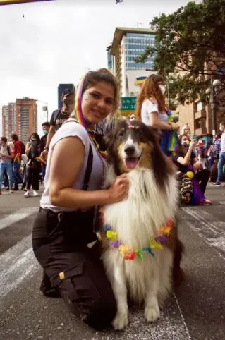 Mujer abraza a un perro collie con una guirnalda de colores durante la Marcha del Orgullo