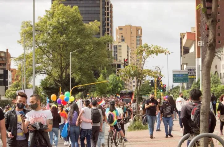Multitud camina por una avenida arbolada con globos de colores durante la Marcha del Orgullo