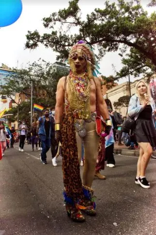 Persona con tocado de plumas y atuendo dorado estampado posa en la calle durante la Marcha del Orgullo