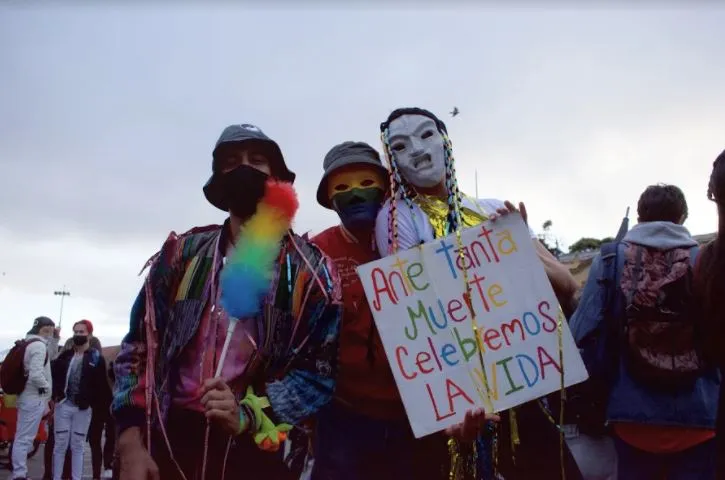 Manifestantes con máscaras y un cartel «Ante tanta muerte celebremos la vida» en la Marcha del Orgullo