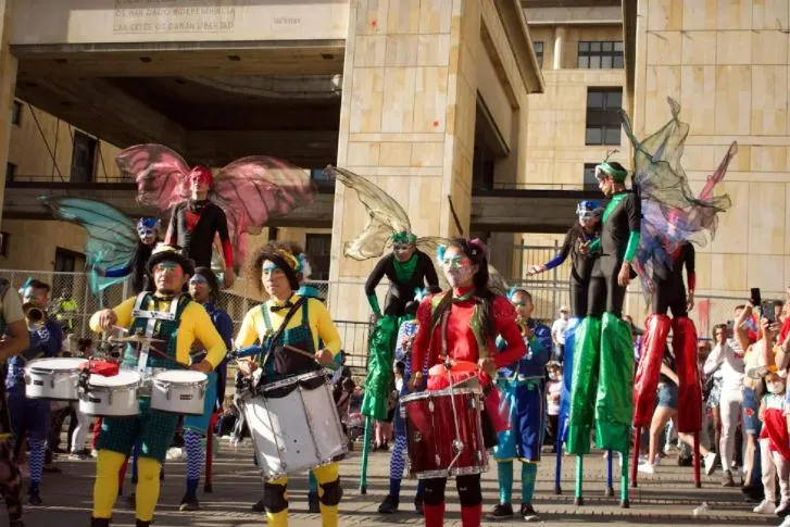 Comparsa con tambores y zancudos con alas de hada frente a un edificio de piedra durante la Marcha del Orgullo