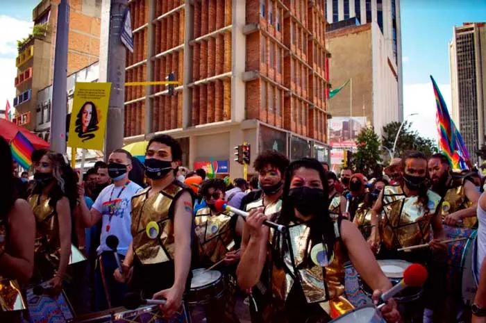 Comparsa de tamborileros con petos dorados y mascarillas avanza entre la multitud de la Marcha del Orgullo