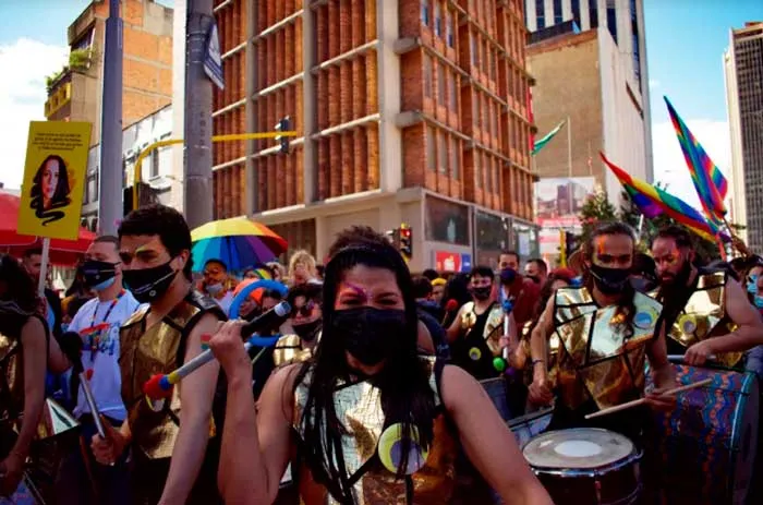 Comparsa de tamborileros con petos dorados y mascarillas avanza entre la multitud de la Marcha del Orgullo
