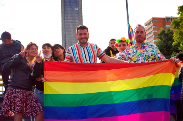 Grupo de personas sonrientes sostiene una gran bandera arcoíris en la Marcha del Orgullo