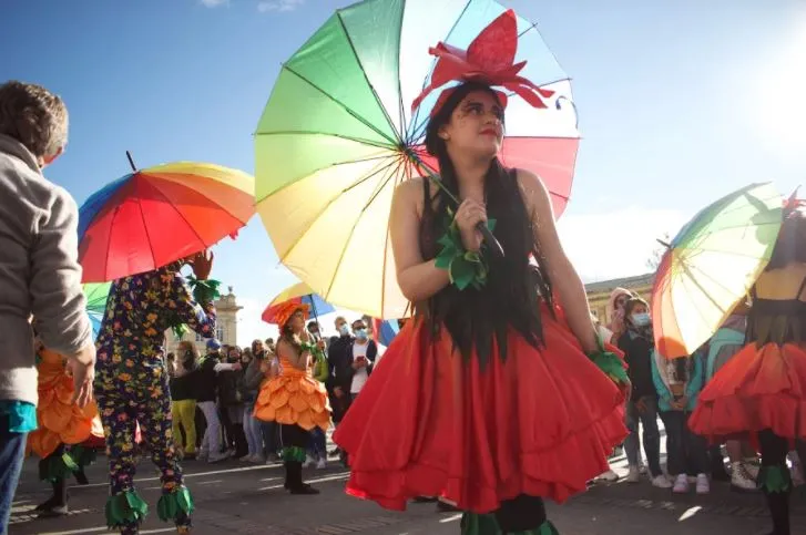Persona con vestido rojo y sombrilla de colores del arcoíris, rodeada de otras sombrillas, en la Marcha del Orgullo