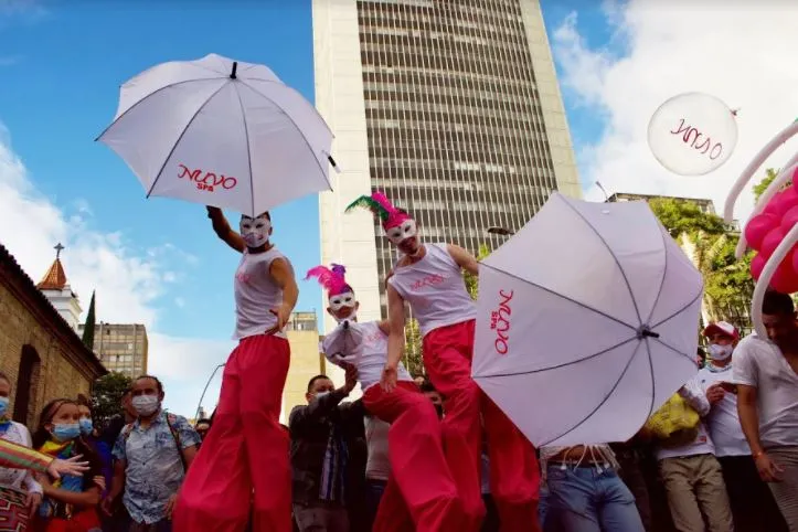 Zancudos con trajes rojos y blancos y sombrillas blancas caminan sobre zancos entre la multitud del Orgullo
