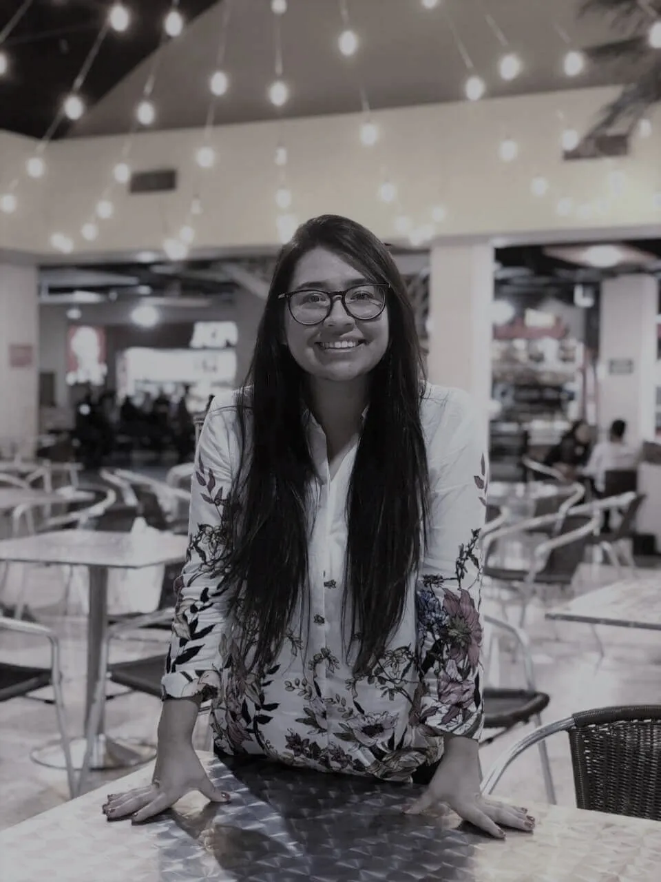 Retrato en blanco y negro de María Paula Macías Acosta, sonriente y con gafas, sentada en una mesa