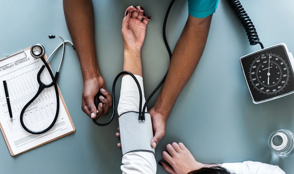 Vista cenital de un médico que toma la presión arterial a un paciente, con estetoscopio y tablilla al lado