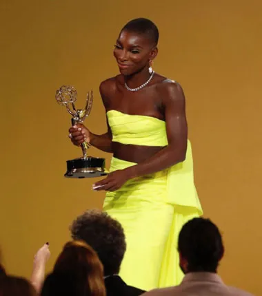 Michaela Coel de vestido amarillo neón sostiene un premio Emmy ante un público