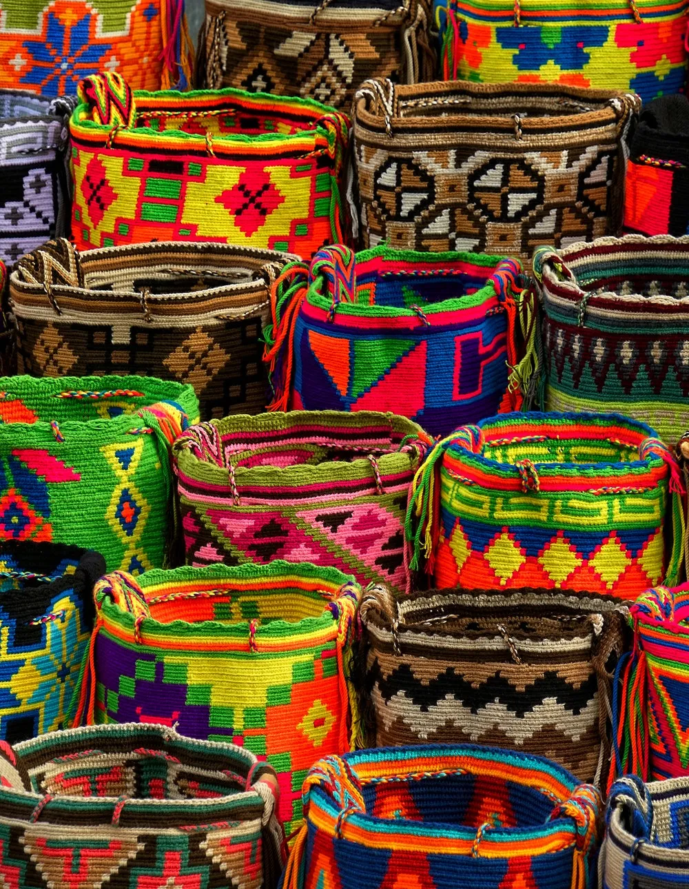 Pila de mochilas artesanales tejidas de colores vivos con diseños geométricos