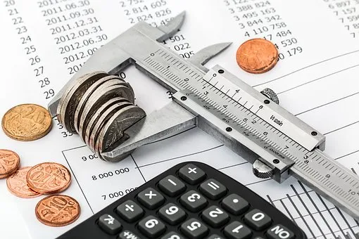 Monedas, un calibrador y una calculadora sobre hojas con cifras, en alusión a presupuesto y leyes