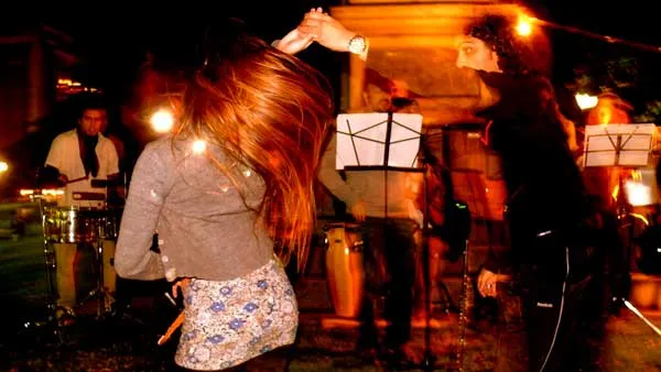 Mujer baila frente a una banda de músicos con atriles en un evento nocturno al aire libre