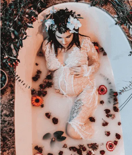 Mujer con flores en el cabello y vestido blanco de encaje recostada en una bañera con leche y pétalos