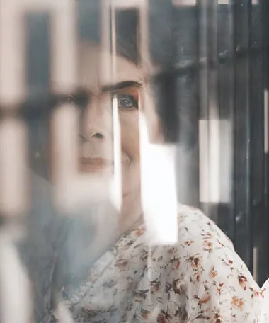 Retrato de una mujer con blusa floral mirando de lado, visto a través de un cristal con reflejos