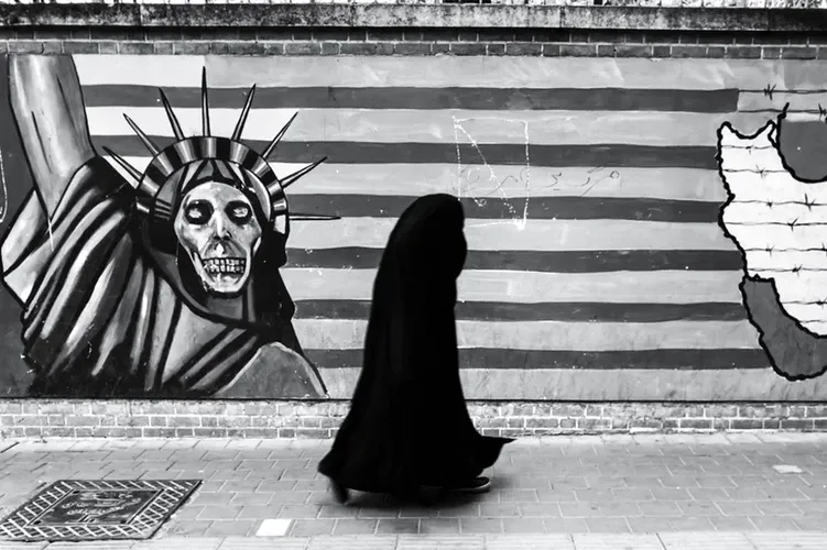 Mujer con burka negra camina frente a un mural con una Estatua de la Libertad calavera sobre la bandera de Estados Unidos