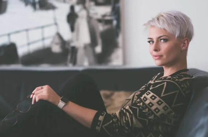 Mujer de cabello corto platinado recostada en un sofá mirando a un lado