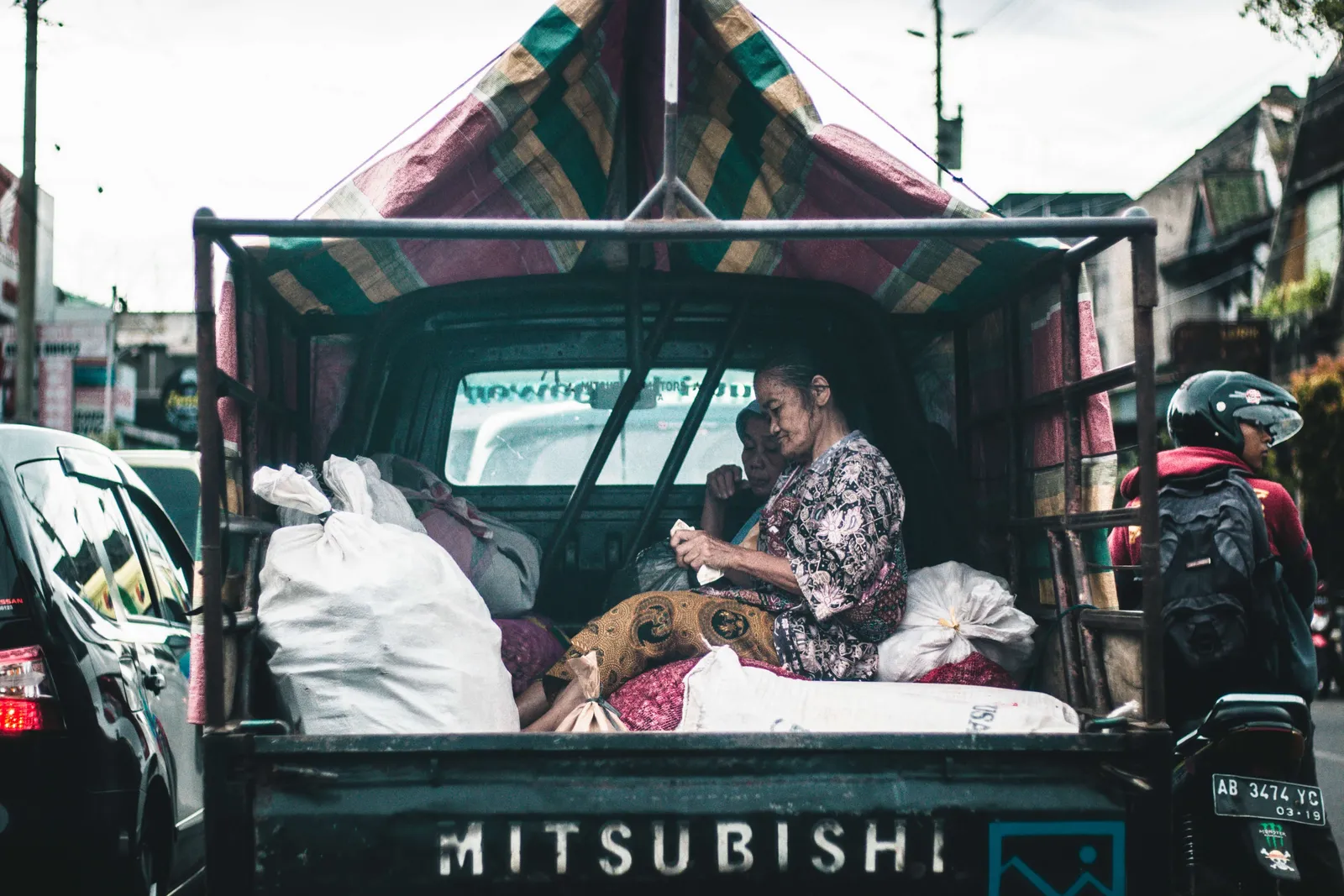 Mujer sentada en la parte trasera de una camioneta Mitsubishi cargada con bultos en una calle