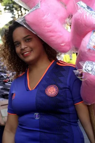 Mujer sonriente con camiseta azul de la selección de Colombia y algodones de azúcar rosados a su espalda