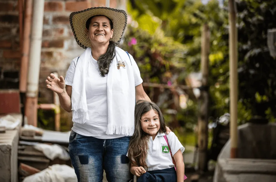 Mujer campesina con sombrero y pañuelo blanco sonríe abrazando a una niña